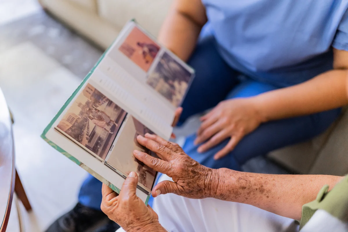 Senior Resident Browsing Photo Album Beside the Caregiver in a Modern Memory Care Facility Senior Resident Browsing Photo Album Beside the Caregiver in a Modern Memory Care Facility