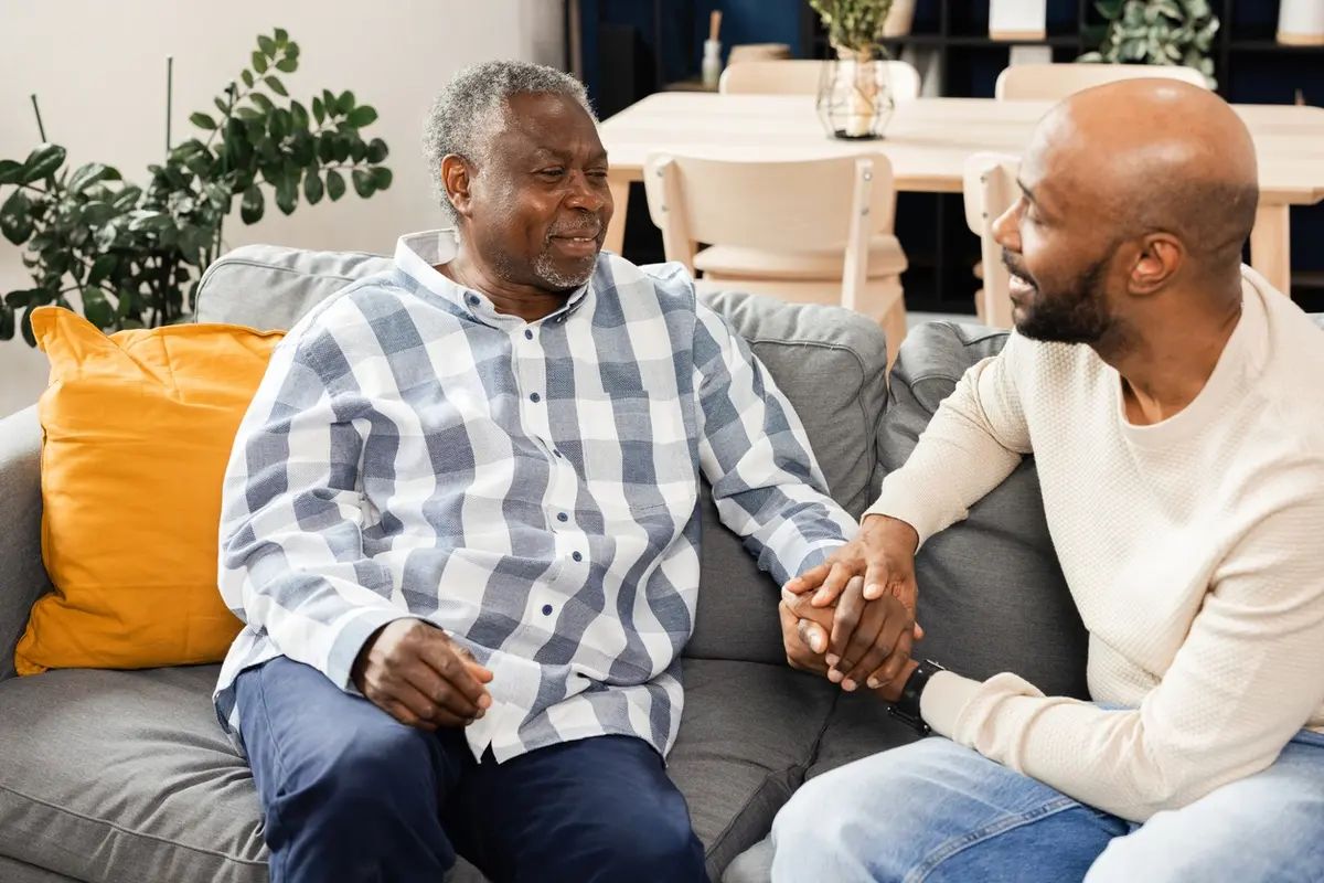 Adult son holds his elderly father’s hand, offering support during a quiet moment at home. What Are 3 Things Not To Say To Someone With Dementia