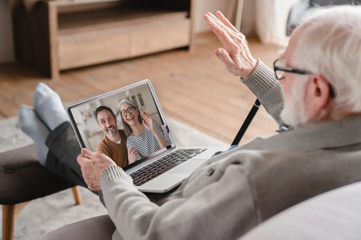 Older man smiling and maintain meaningful connections while on a video call with family using a laptop at home.