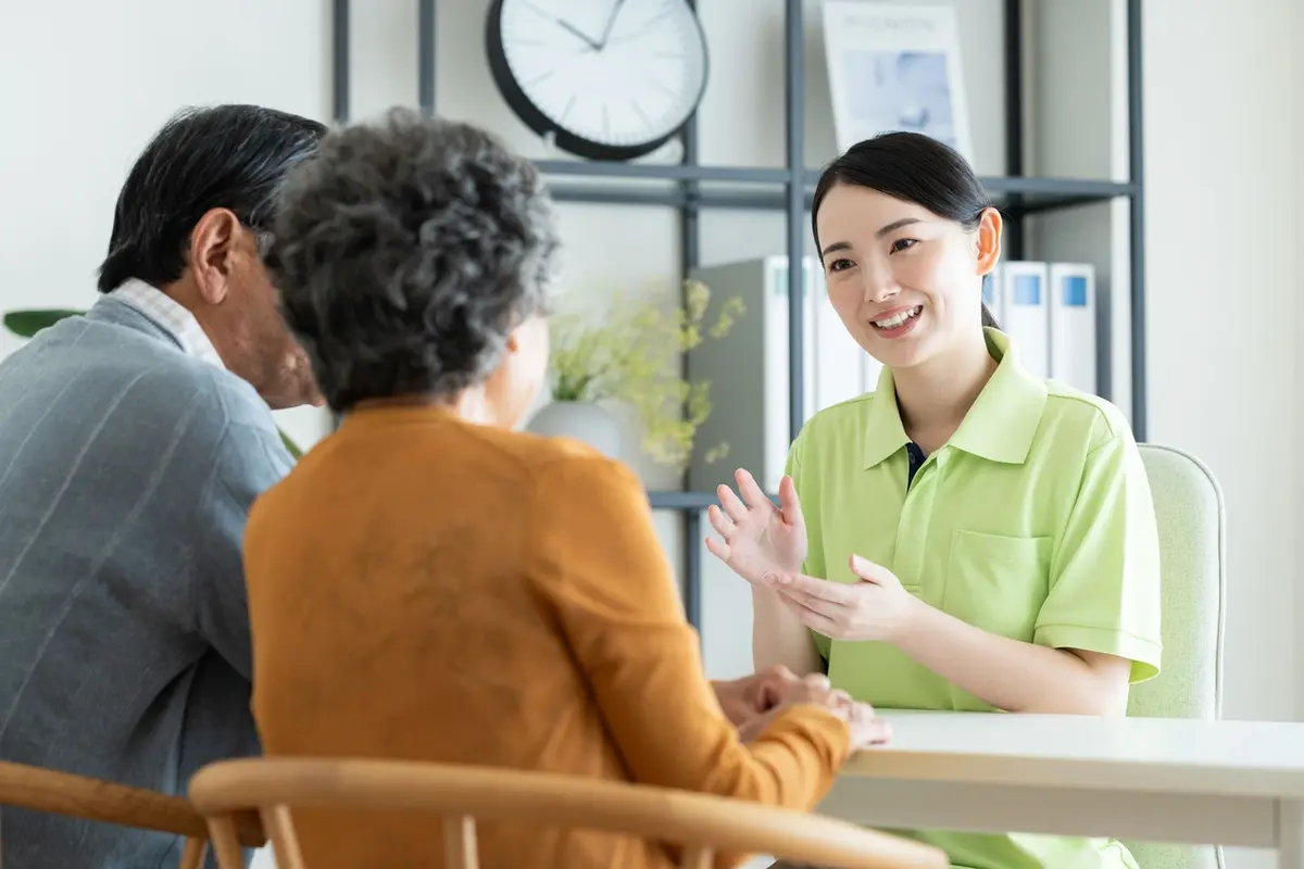 A professional caregiver sits and speaks with an elderly couple in a warmly lit family home, representing a compassionate assisted living consultation