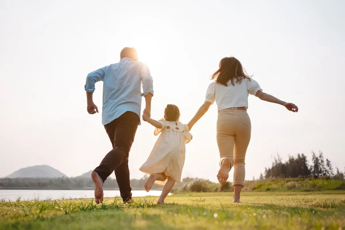 A happy family runs and walks together in a park at sunset, representing how to avoid caregiver stress through consistent daily habits, shared family support, and protecting time for personal wellbeing.
