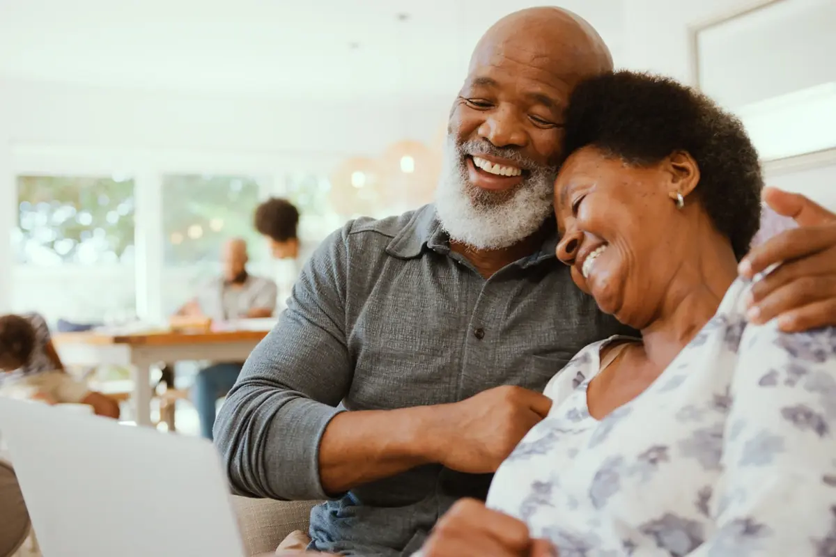 A senior couple sits at home reviewing assisted living options on a laptop alongside adult family members, representing a multigenerational family researching questions to ask when looking for assisted living communities.
