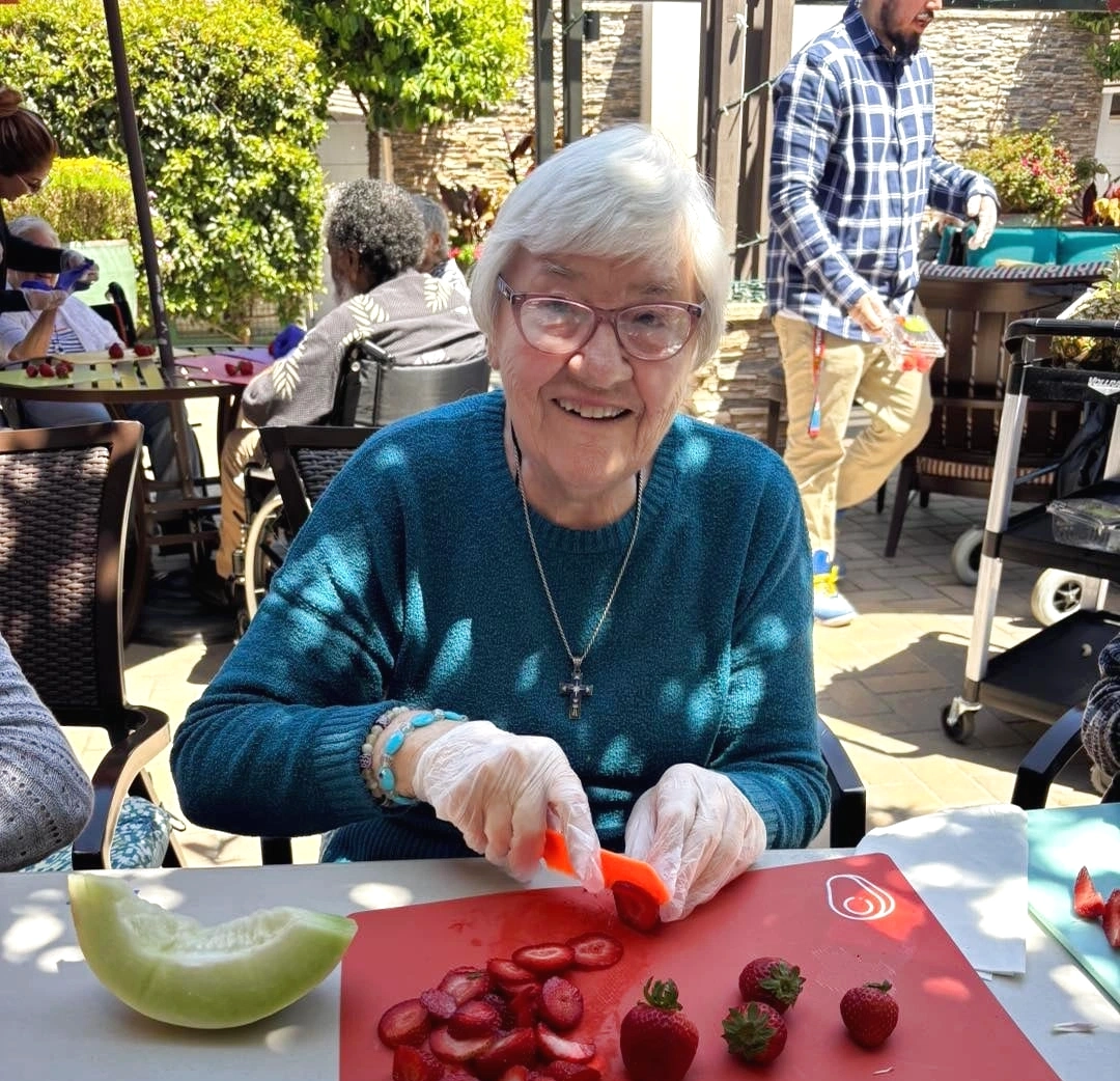 Outdoor Spaces in Assisted and Memory Care Patio Activity Outdoor spaces in assisted and memory care: senior slices strawberries during patio activity safely.