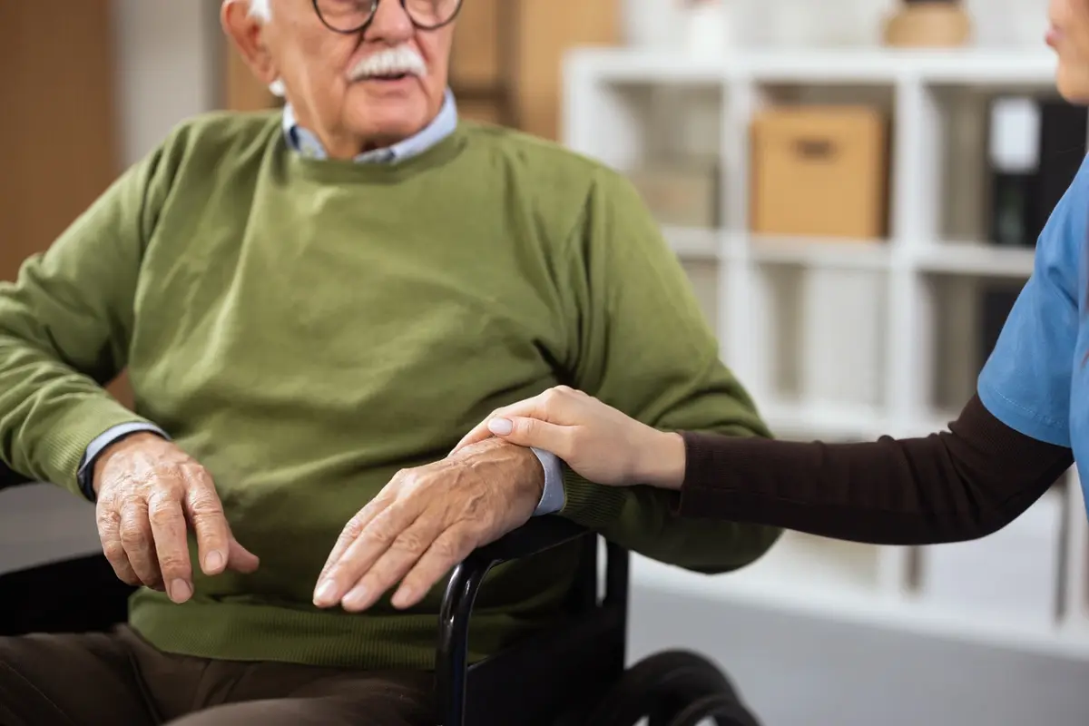 Caregiver holding a senior man’s hand, showing the risks of hiring a private caregiver.