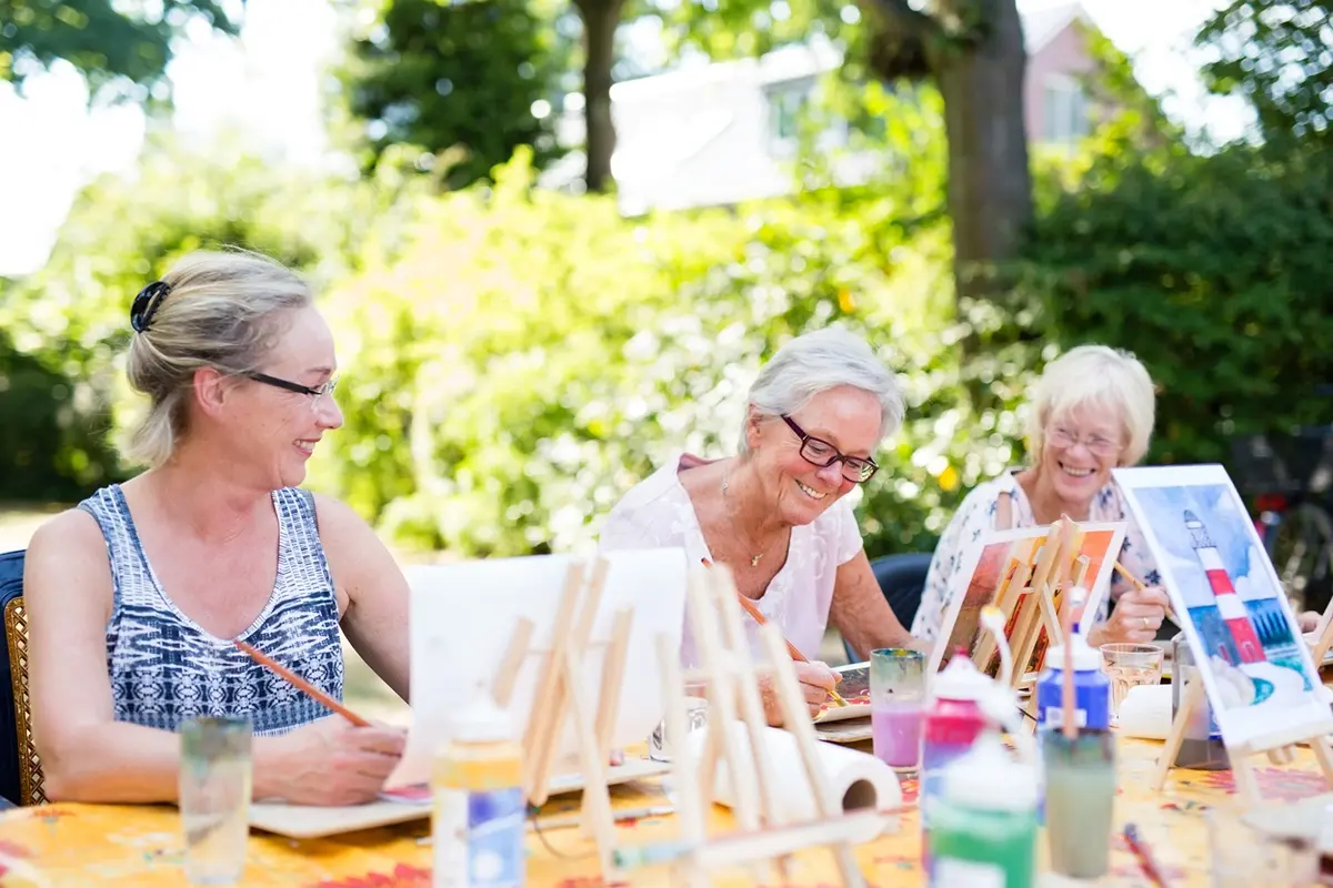 Older women attending an outdoor art class, representing the benefits of community care for safe, social summer engagement.